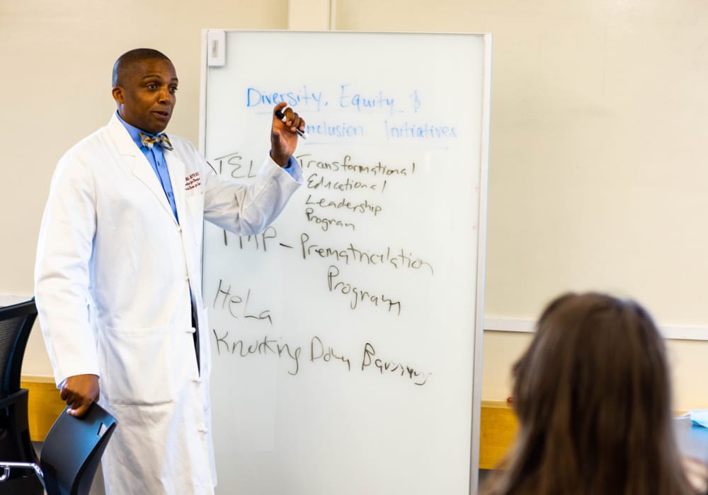 Dr. Mill Etienne standing in front of a whiteboard he is writing on as he conducts a lecture on diversity